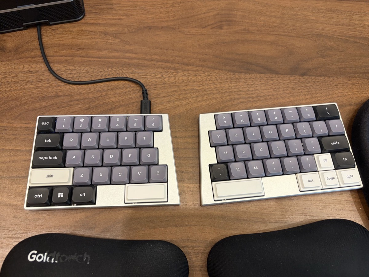 ElimKeys Elytra split keyboard in white with full-size grey and cream keycaps, showing the remapped tilde key on the right half